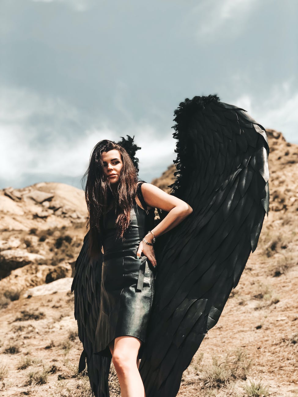 model in a leather mini dress with black feather wings among the barren hills